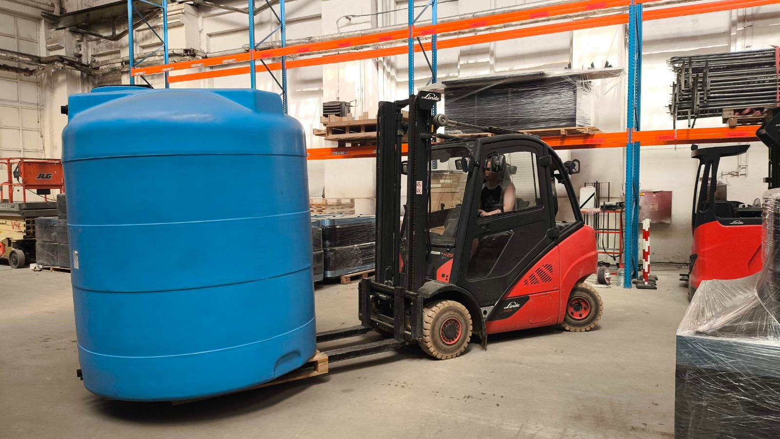 Погрузчик Linde перевозит на паллете большую пластиковую ёмкость по складу